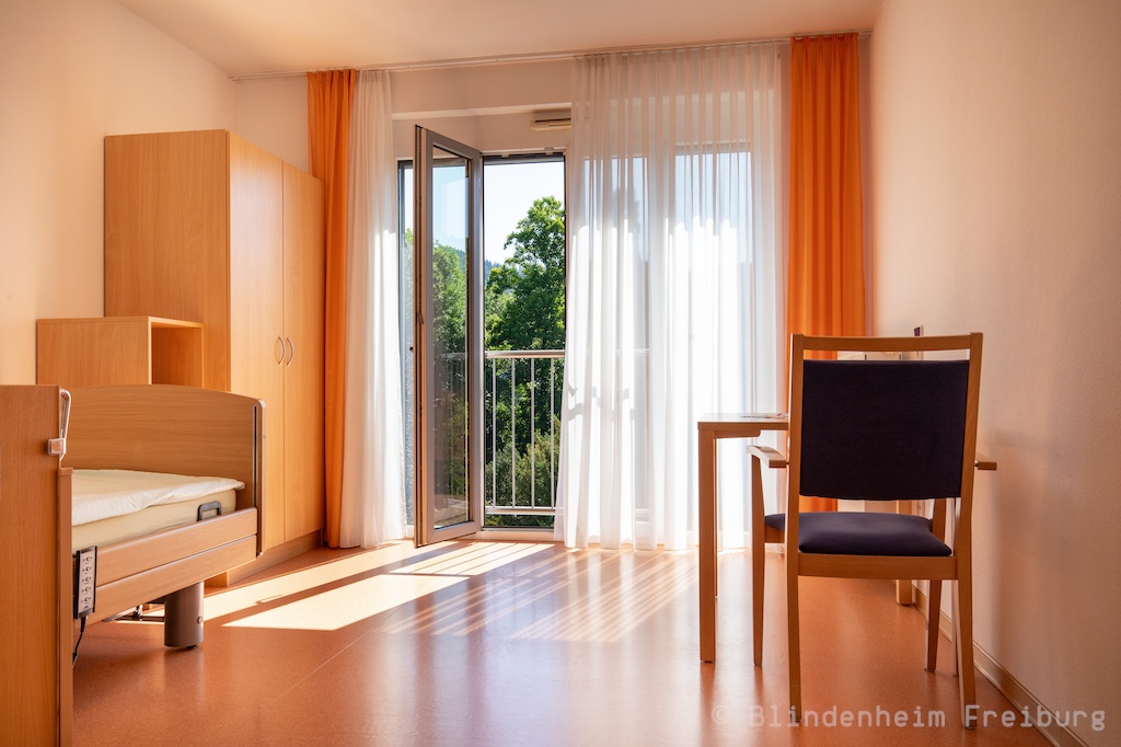 Blindenheim Freiburg freies Zimmer mit Bett, Schrank, Tisch und Stuhl